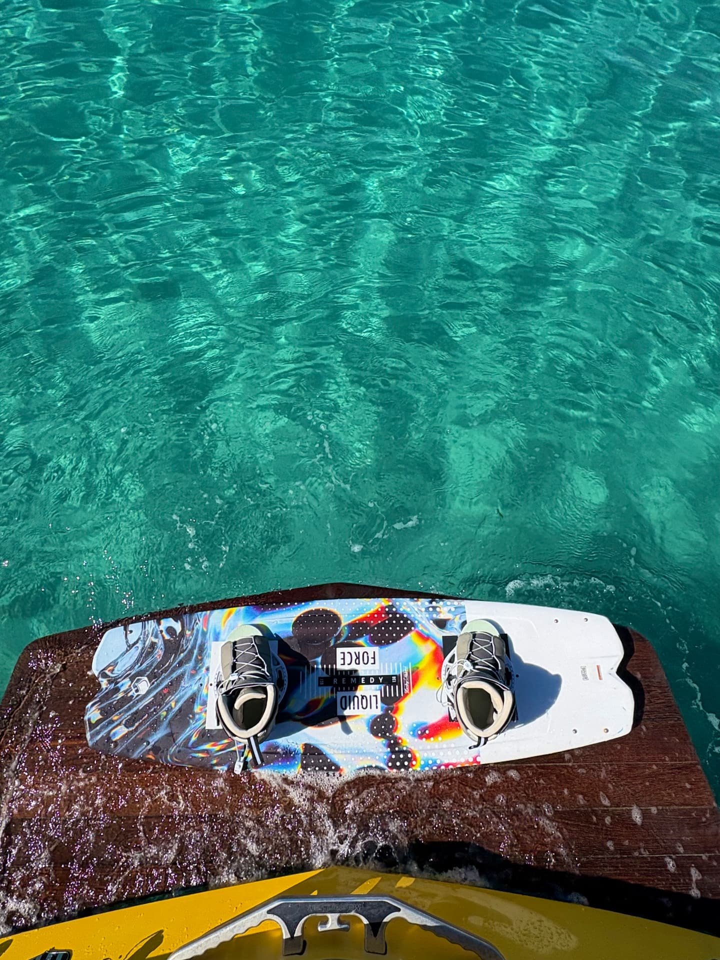 A wakeboard resting on the swim platform of the boat above turquoise water